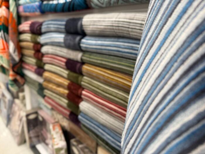 Assorted folded striped fabric rolls on a shelf in multiple colours
