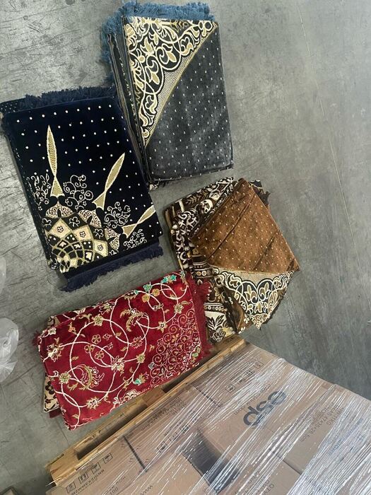 Assorted folded prayer mats in navy, grey, brown and red patterns