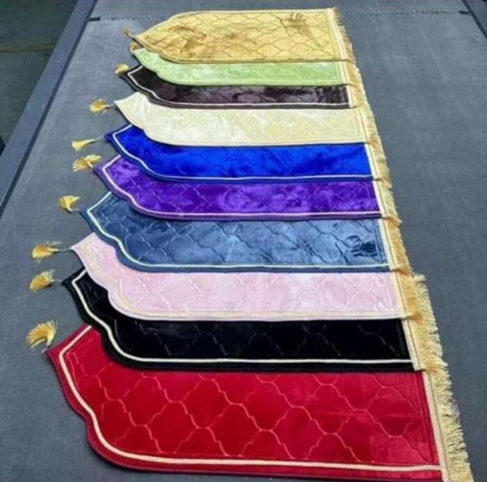 Multicoloured velvet prayer rugs with tasselled edges arranged in a row